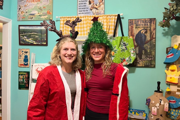Two women in festive hats and attire, smiling in a room with colorful wall decor.