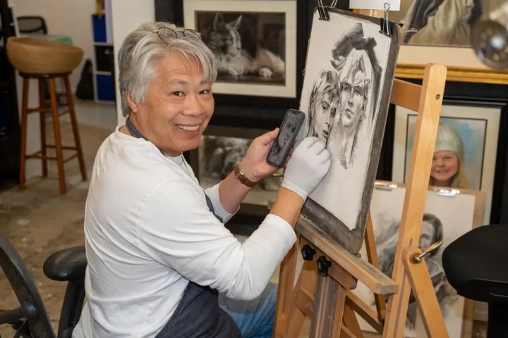 Artist smiling while drawing a portrait on an easel in a studio.