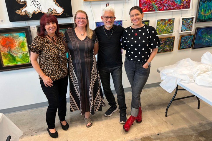 Four people posing in an art gallery with colorful paintings on the wall.