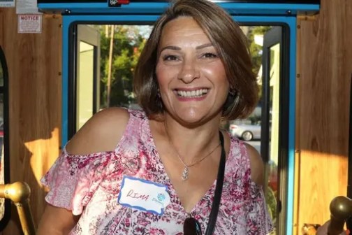 Smiling person standing inside a bus with colorful poles.