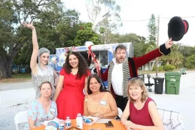 Group of five people in festive attire posing outdoors at a table.