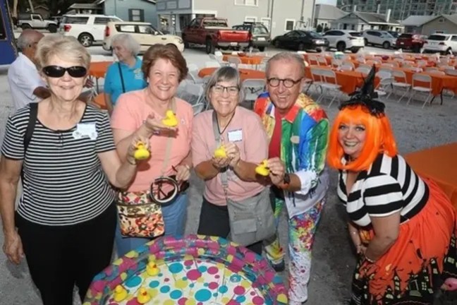Group of five people smiling, holding rubber ducks at an outdoor event.