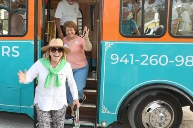 Smiling woman in hat exits colorful bus, followed by two people.