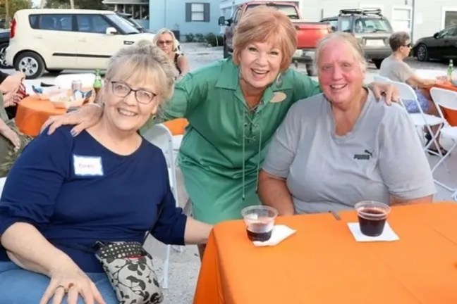 Three women smiling at an outdoor table with drinks.