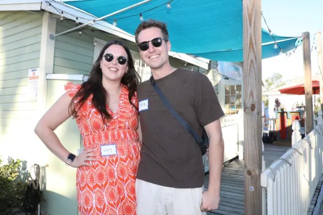Smiling couple wearing name tags standing outdoors by a green building.