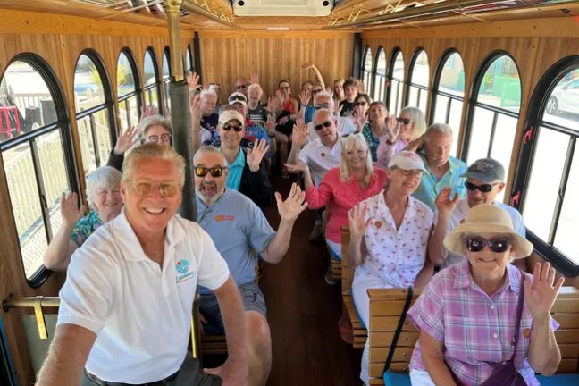 Group of people smiling and waving inside a trolley.