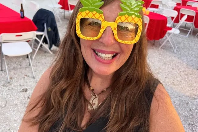Woman smiling, wearing pineapple-shaped glasses at an outdoor event.