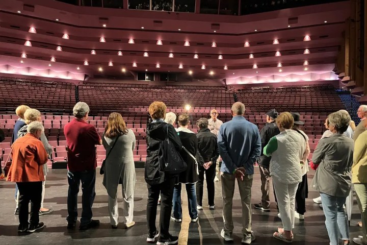 People standing on stage facing empty theater seats.