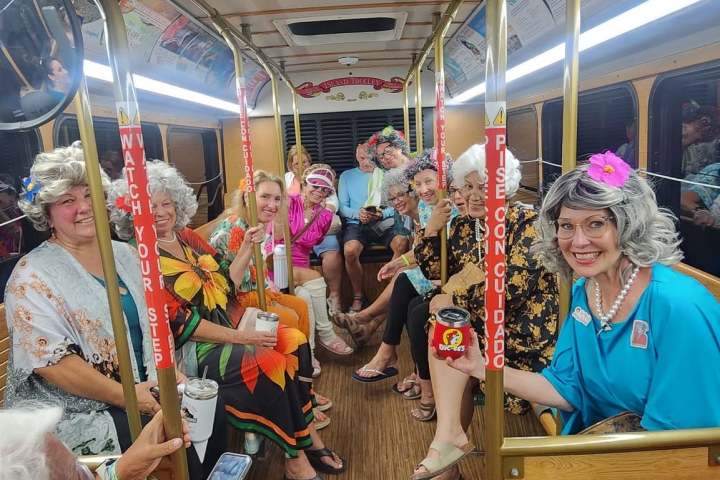 Group of people in a vintage bus, smiling and wearing colorful outfits and hats.