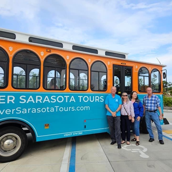 Four people stand in front of a turquoise tour bus labeled 'Discover Sarasota Tours.'