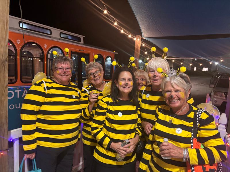 Group of people in bee costumes posing outdoors at night.