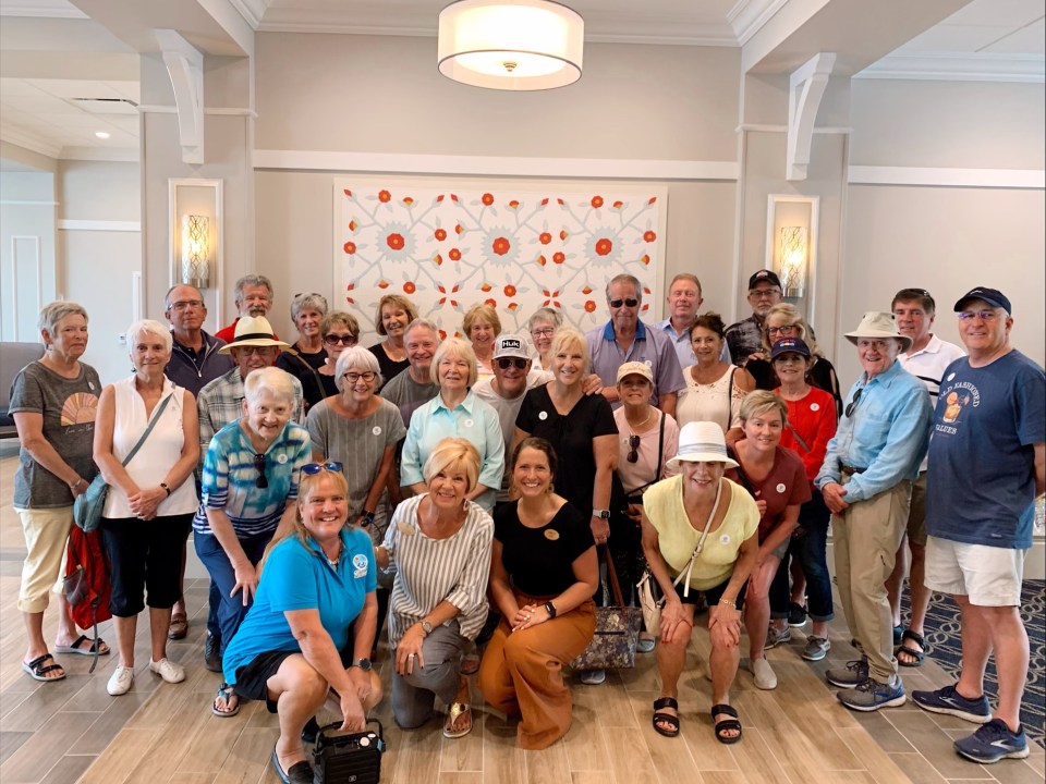 Group of smiling people posing indoors in front of a decorative wall.