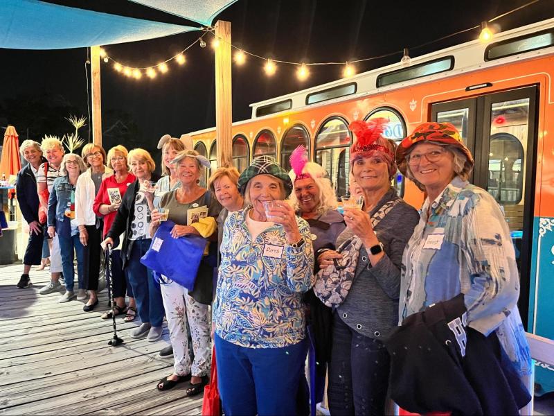 Group of people posing on a wooden deck at night by an orange bus with festive lights.