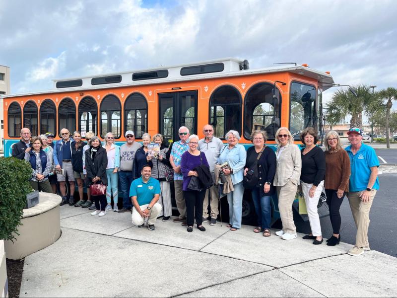 Group of people posing in front of an orange trolley bus.