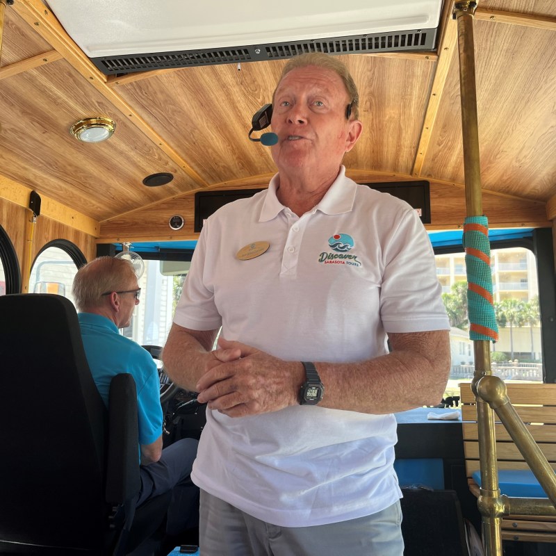 Man wearing a white polo shirt speaking inside a vintage trolley car.