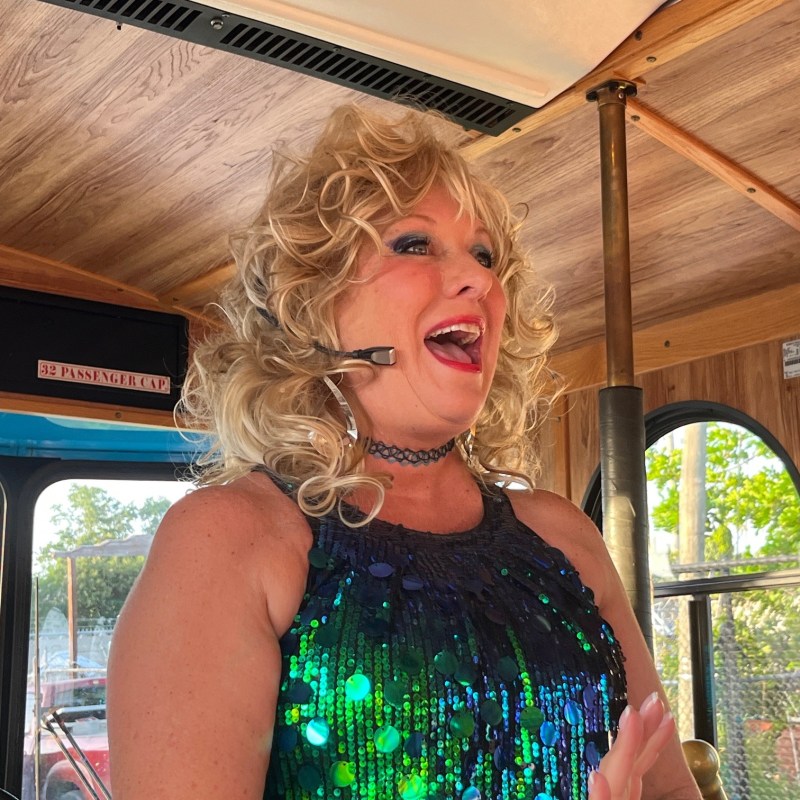 Person in a sequin dress, wearing a headset, speaking on a bus.