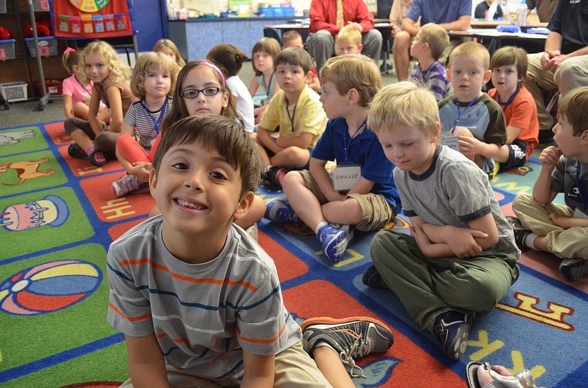 Children sitting cross-legged on a colorful classroom rug, smiling and listening.