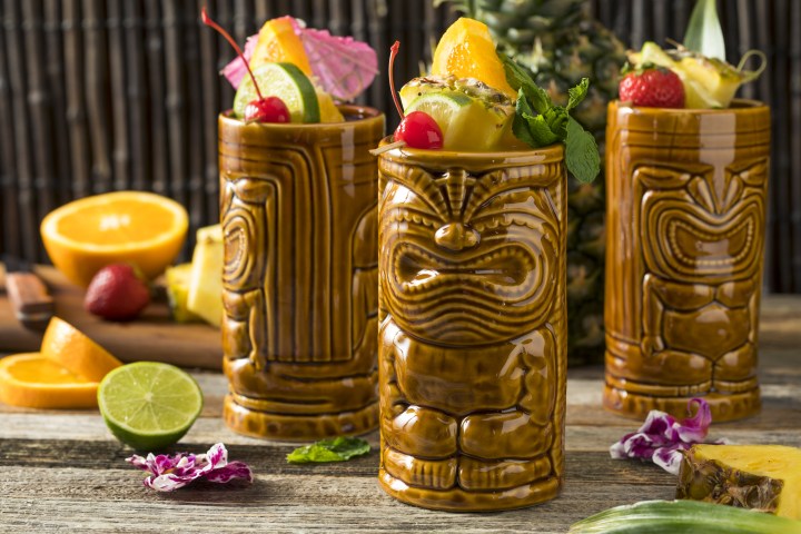 Three tiki mugs filled with tropical fruit and garnishes.