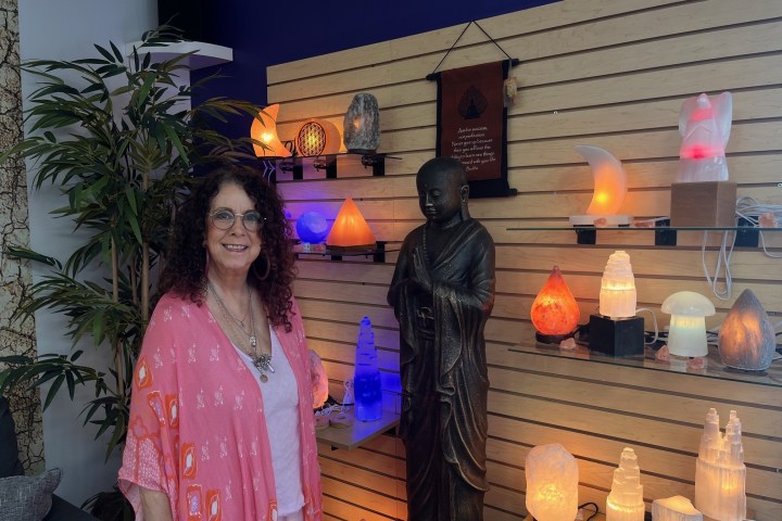 Woman in a pink shawl stands beside lit salt lamps and a Buddha statue.