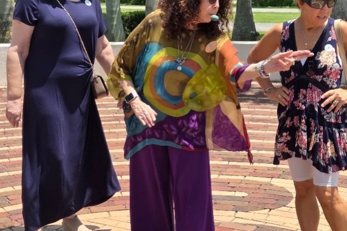 Three women on a brick path, one wearing a colorful outfit, mid-conversation.